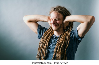 Young Man With Dreadlocks Blocking His Ears On A Solid Background