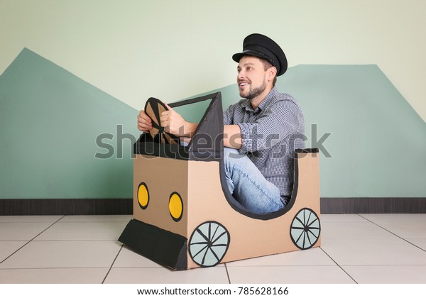 Young man dreaming of buying own auto while\
playing with cardboard car\
indoors