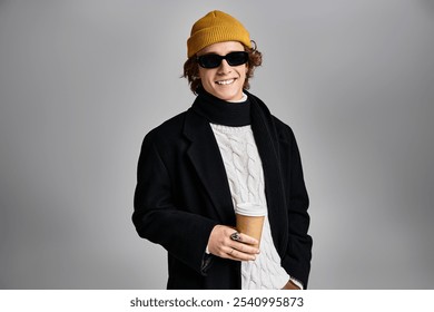 A young man dressed in a black coat and yellow beanie holds a coffee cup, exuding style in a contemporary setting. - Powered by Shutterstock