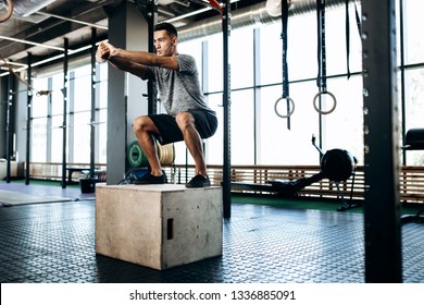 Young man dressed in black sports clothes is doing squats on the box next to the sport equipment in the gym - Powered by Shutterstock