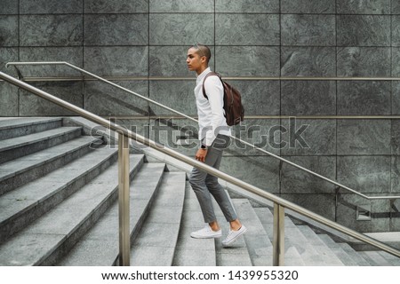 Young man dressed in casual clothes and backpack in the city center is going up the stairs - Millennial is going to work