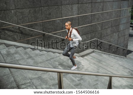 Young man dressed in casual clothes and backpack in the city center is going up the stairs - Millennial is going to work