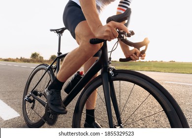 Young Man Dressed In White T-shirt And Black Shorts Cycling On Paved Road. Close Up Of Strong Male Legs And Hands. Concept Of Favorite Hobby.