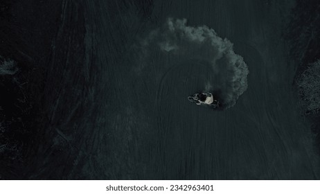 A young man drifts on a motorcycle on black volcanic lava, top view. Drift on volcanic sand, clouds of sand rise. Spectacular stunts on a motorcycle in the sand.