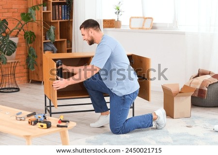 Young man with drill assembling chest of drawers at home
