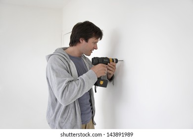 Young Man Drilling Hole In The Wall