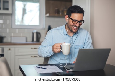 Young man drink coffee while wearing earphones and having a video call on laptop.