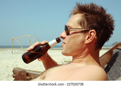 Young Man Drinking Beer On The Beach