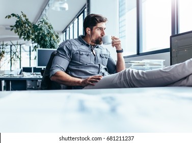 Der junge Mann trinkt während der Pause im Büro Kaffee. Geschäftsmann hört Musik mit einer Tasse Kaffee.