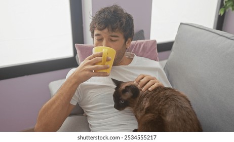 Young man drinking coffee and petting siamese cat on sofa in cozy living room - Powered by Shutterstock