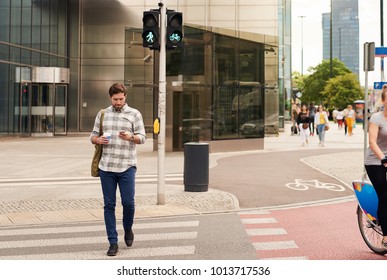 Young man drinking a coffee and sending a text message on a cellphone while crossing a street in the city  - Powered by Shutterstock