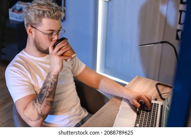 Young man drinking coffee while working with laptop late in evening