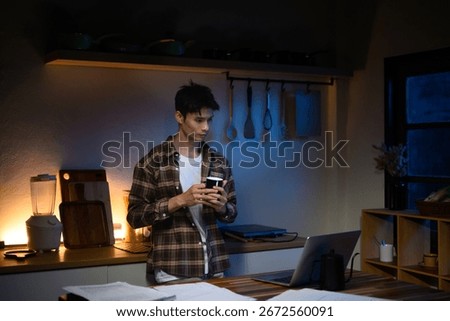 Young man drinking coffee while working late on a laptop in the kitchen