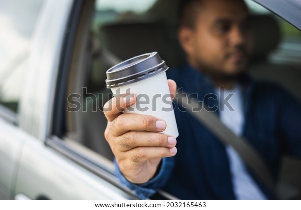 Young man drinking a cup of hot\
coffee while driving car to travel. Hands holding steering\
wheel.