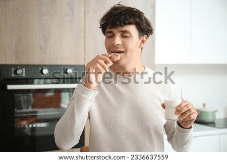 Young man drinking fresh milk and eating cookie in kitchen