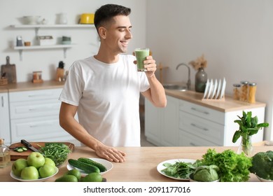 Young Man Drinking Healthy Green Smoothie In Kitchen