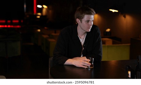 Young man drinking whiskey while sitting in a restaurant in the evening and feeling lonely. Lifestyle, loneliness concept.