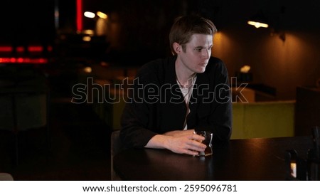 Young man drinking whiskey while sitting in a restaurant in the evening and feeling lonely. Lifestyle, loneliness concept.
