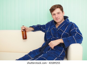 The Young Man Drinks Beer In A Dressing Gown On A Sofa