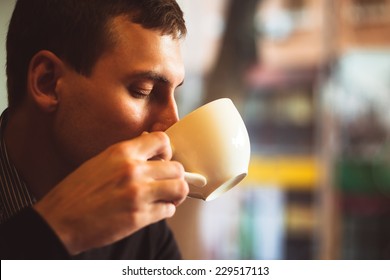 Young man drinks coffee on the street. Man drinks coffee. Young man drinks coffee outdoor. Businessman drinks coffee outdoor. Man drink coffee in cafe. Cozy atmosphere. Student drinks coffee. Coffee - Powered by Shutterstock
