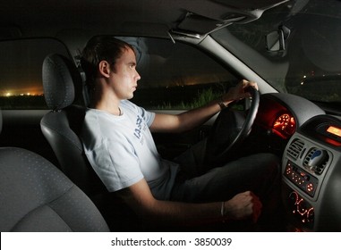 Young Man Driving A Car At Night. Interior Of A Car.