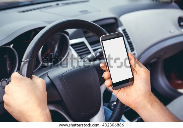 Young man driving a car with a phone in\
his hand. Multitasking. Don\'t text and\
drive
