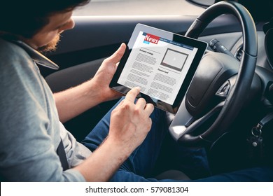 Young Man Driving A Car With A Tablet In Hand, Talking On Mobile Phone. Multitasking. Safe Driving Concept