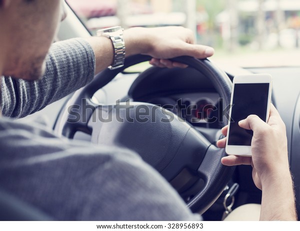 Young man driving\
car and using mobile\
phone