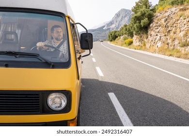 Young man driving his retro yellow camper van on a mountainous coastal road in Croatia - Powered by Shutterstock