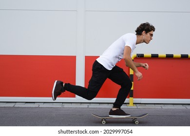 Young Man Driving Skateboard Outdoor Against Red And White Wall. In A Hurry Concept