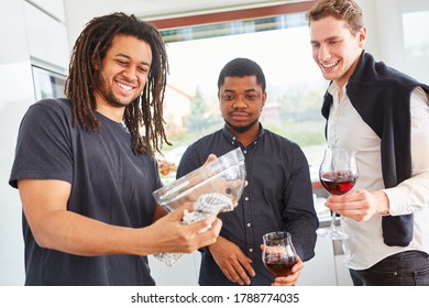 Young Man Drying Dishes With Tea Towel In Kitchen Next To Friends With Red Wine