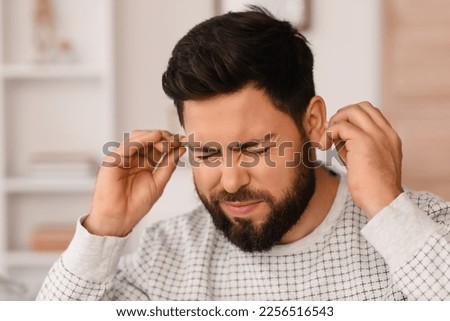 Young man with ear plugs suffering from loud noise at home, closeup