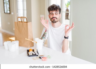 Young man eating asian sushi from home delivery relax and smiling with eyes closed doing meditation gesture with fingers. Yoga concept.