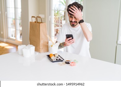 Young Man Eating Asian Sushi From Home Delivery And Ordering Food Using Smartphone App Stressed With Hand On Head, Shocked With Shame And Surprise Face, Angry And Frustrated. Fear And Upset