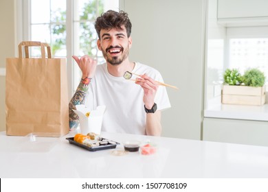 Young man eating asian sushi from home delivery pointing and showing with thumb up to the side with happy face smiling - Powered by Shutterstock