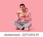 Young man eating Chinese noodles on pink background