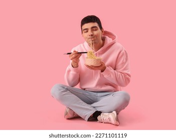 Young man eating Chinese noodles on pink background