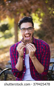 Young man eating a cookie, looking happy at the camera. Hipster style, wearing a check shirt