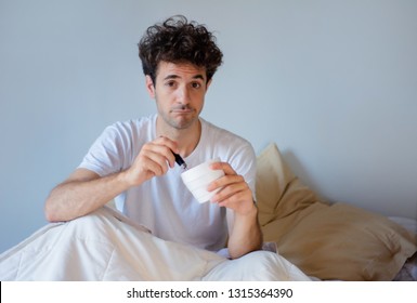 Young Man Eating Ice Cream While Resting In The Bed At Home. Indoors 