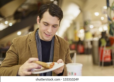 Young Man Eating Pizza At The Food Court In A Mall