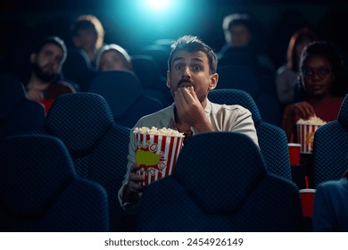 Young man eating popcorn while watching movie in disbelief in cinema. - Powered by Shutterstock