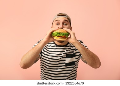 Young Man Eating Tasty Burger On Color Background