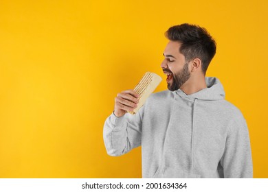 Young man eating tasty shawarma on yellow background. Space for text - Powered by Shutterstock