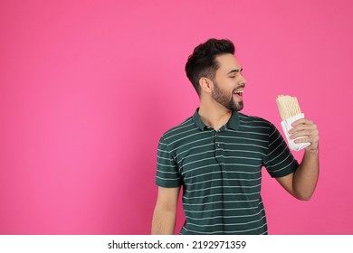 Young man eating tasty shawarma on pink background. Space for text