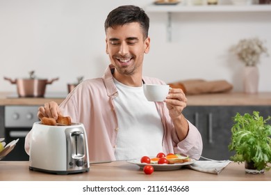 Young man eating tasty toasts and drinking coffee in kitchen - Powered by Shutterstock