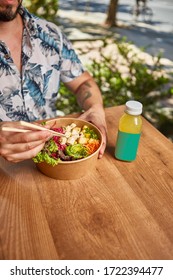 Young Man Eating Traditional Organic Poke Bowl Of Salmon, Shrimp, Avocado, Rice, Vegetables Placed On Textured Backgrounds.