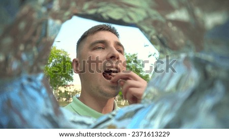 A young man eats potato chips from a packet while walking in the park. View of a man from a bag of chips.