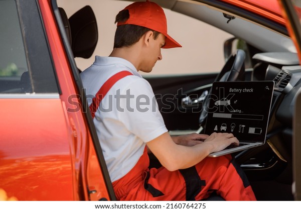 Young man electric car mechanic is using an laptop\
computer to check diagnostic the electrocar errors and problems and\
fix it. \
