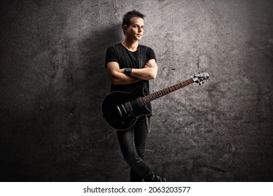 Young Man With An Electric Guitar On A Strap Leaning On A Gray Rugged Wall 