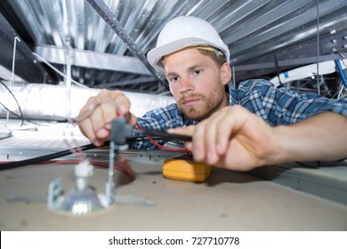 young man electrician wiring inside ceiling